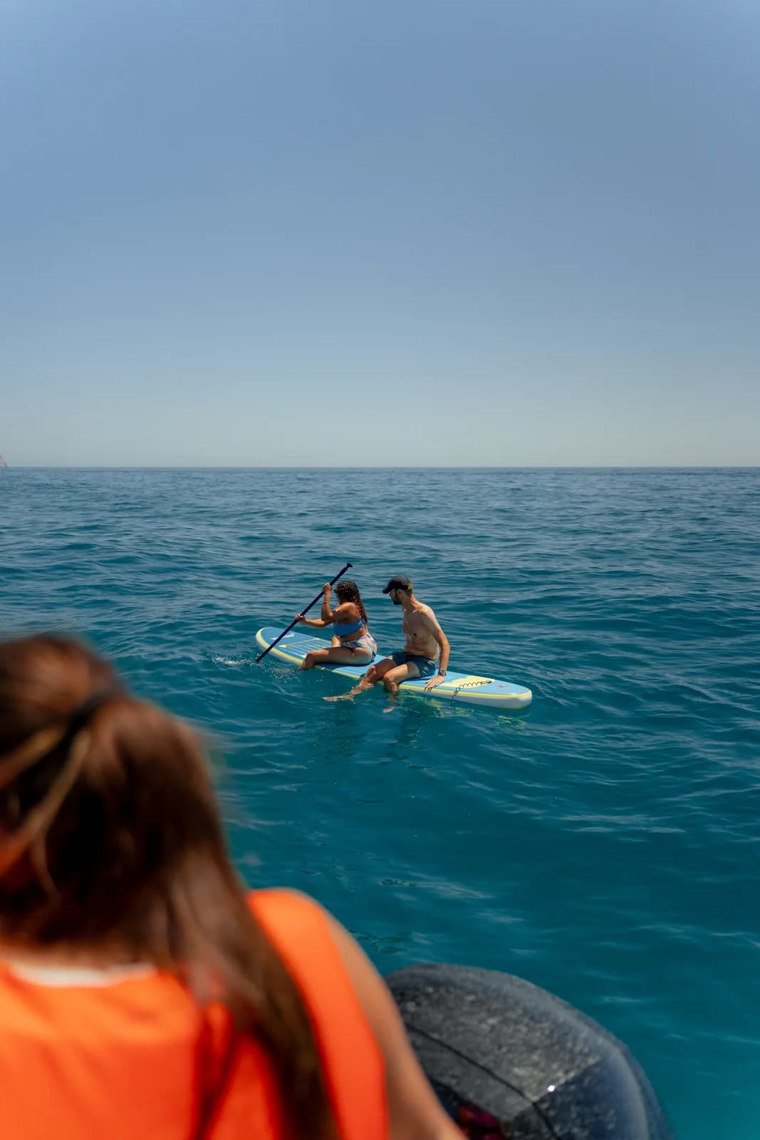 Pasajeros mirando a una tabla de pádel surf desde la borda.