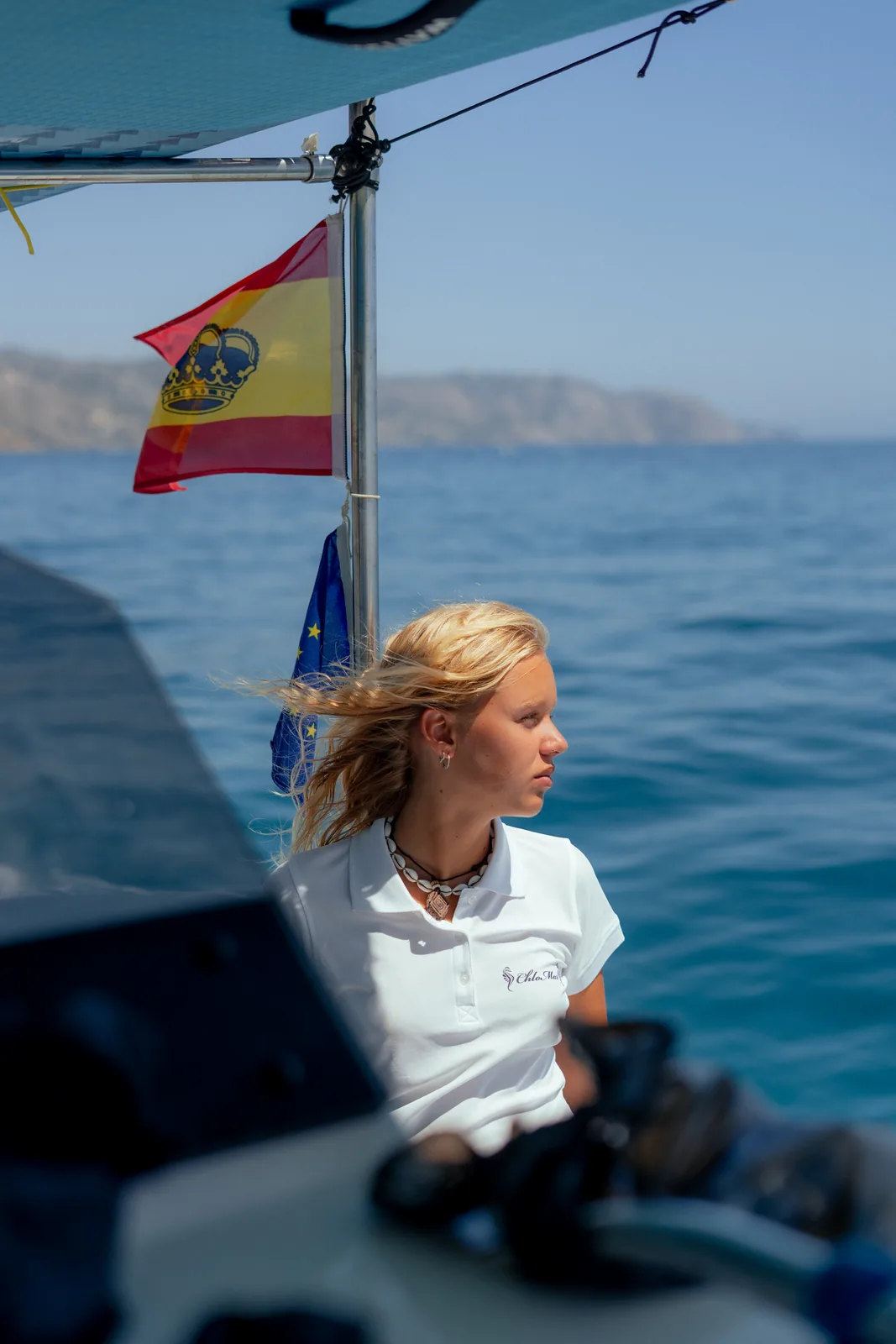 Tripulante a bordo con la bandera y la costa al fondo.